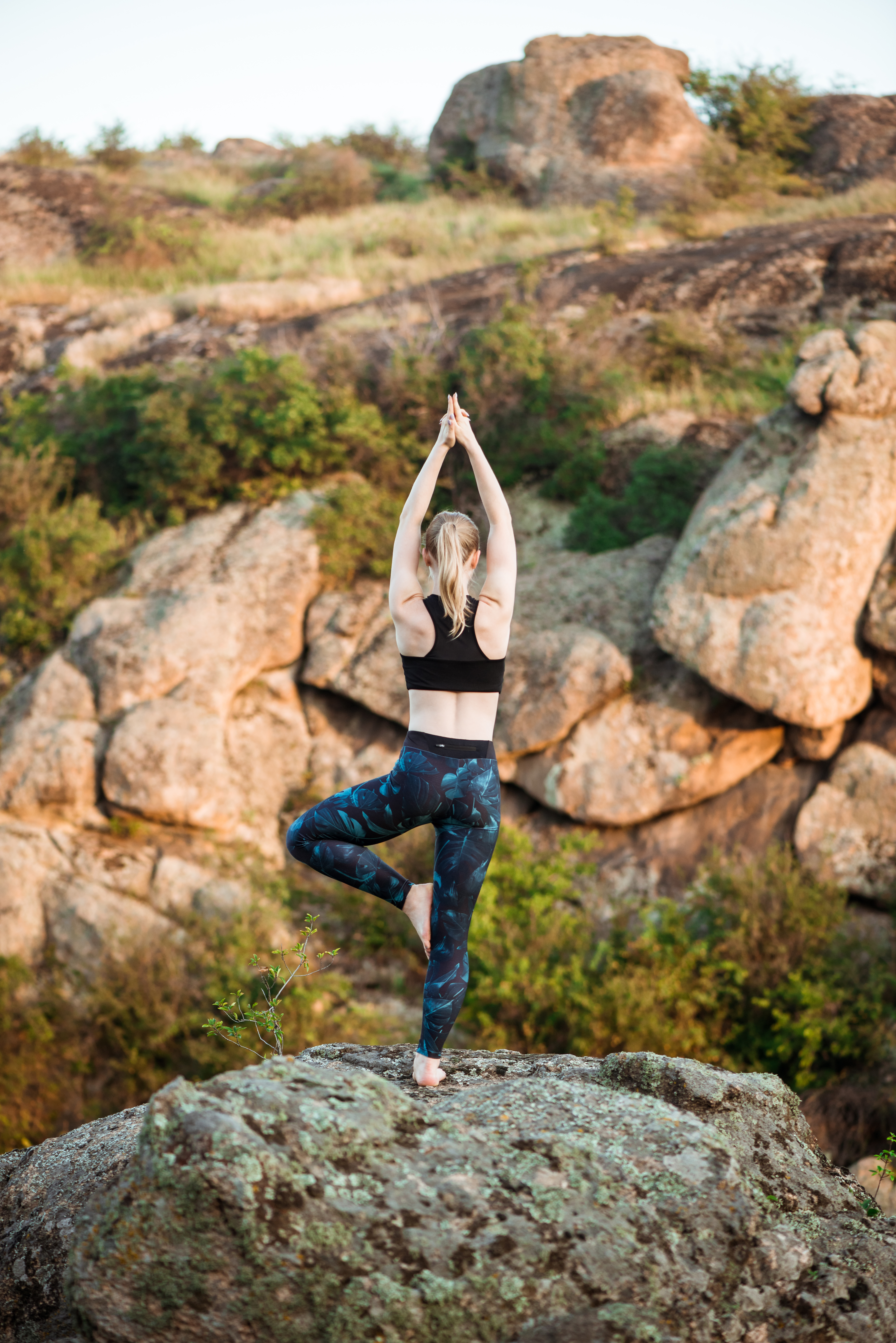 Young sportive girl training yoga asanas on rock in canyon.